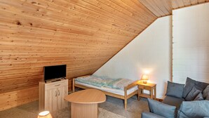 Een gezellige kamer met een schuine kap, een bed, een bank, een televisie en een kleine tafel.