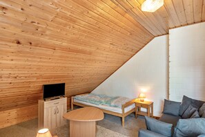 Una habitación acogedora con techo inclinado, una cama, un sofá, un televisor y una mesita.