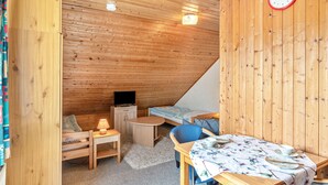 Een houten kamer met een bed, een bureau, een stoel, een televisie en een klok aan de muur.