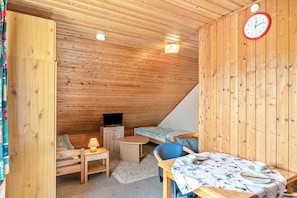 Una habitación de madera con una cama, un escritorio, una silla, un televisor y un reloj en la pared.
