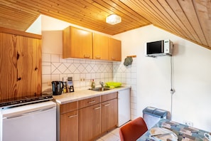 A compact kitchen with wooden cabinets, a microwave, and a small dining area with a table and chairs. - Vacation at the uhlenhoff apartment bansmeer (Ihlow)