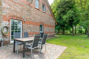 A brick house with a patio, a table with chairs, and a garden. - Vacation at the uhlenhoff apartment ihler meer (Ihlow)