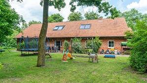 A brick building with a tiled roof, a swing set, and a play area. - Vacation at the uhlenhoff apartment ihler meer (Ihlow)