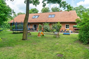 A brick building with a tiled roof, a swing set, and a play area. - Vacation at the uhlenhoff apartment ihler meer (Ihlow)