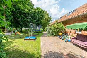 Eine gepflasterte Terrasse mit Schaukel, Spielbereich und überdachter Sitzgelegenheit.