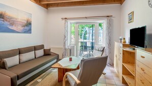 A cozy living room with a sofa, a wooden coffee table, a chair, a TV, and a window with curtains. - Vacation at the uhlenhoff apartment ihler meer (Ihlow)