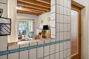 Ein Zimmer mit Holzboden, Fliesenwänden, einem Schreibtisch mit Stuhl, einem Fernseher und einer Tür.
