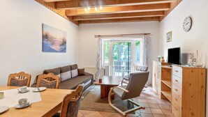 A cozy living room with a wooden ceiling, a painting on the wall, a dining table with chairs, a sofa, a television, and a window with curtains. - Vacation at the uhlenhoff apartment ihler meer (Ihlow)
