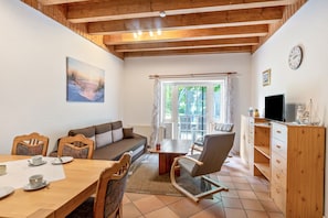 Un salón acogedor con techo de madera, un cuadro en la pared, una mesa de comedor con sillas, un sofá, un televisor y una ventana con cortinas.