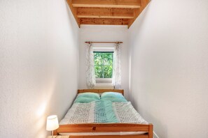 Une petite pièce avec un lit, une fenêtre avec des rideaux, une lampe et un plafond en bois.