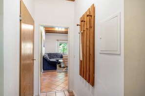 Un couloir avec une porte en bois, une étagère en bois fixée au mur, et un espace de vie comprenant un canapé et une fenêtre.