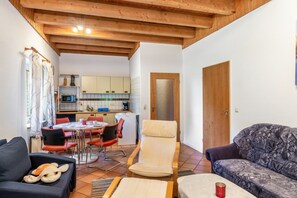 Un'accogliente zona giorno con divano, poltrona, tavolo da pranzo con sedie, una cucina sullo sfondo e un soffitto in legno.