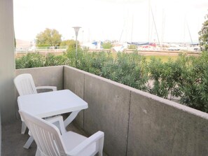 Un balcón con una mesa y sillas blancas, vista a barcos y follaje.