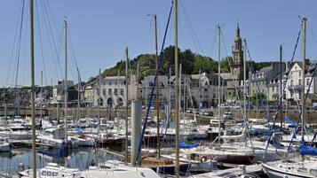 A marina with numerous boats docked, a prominent building with a tower, and a hillside with greenery in the background.