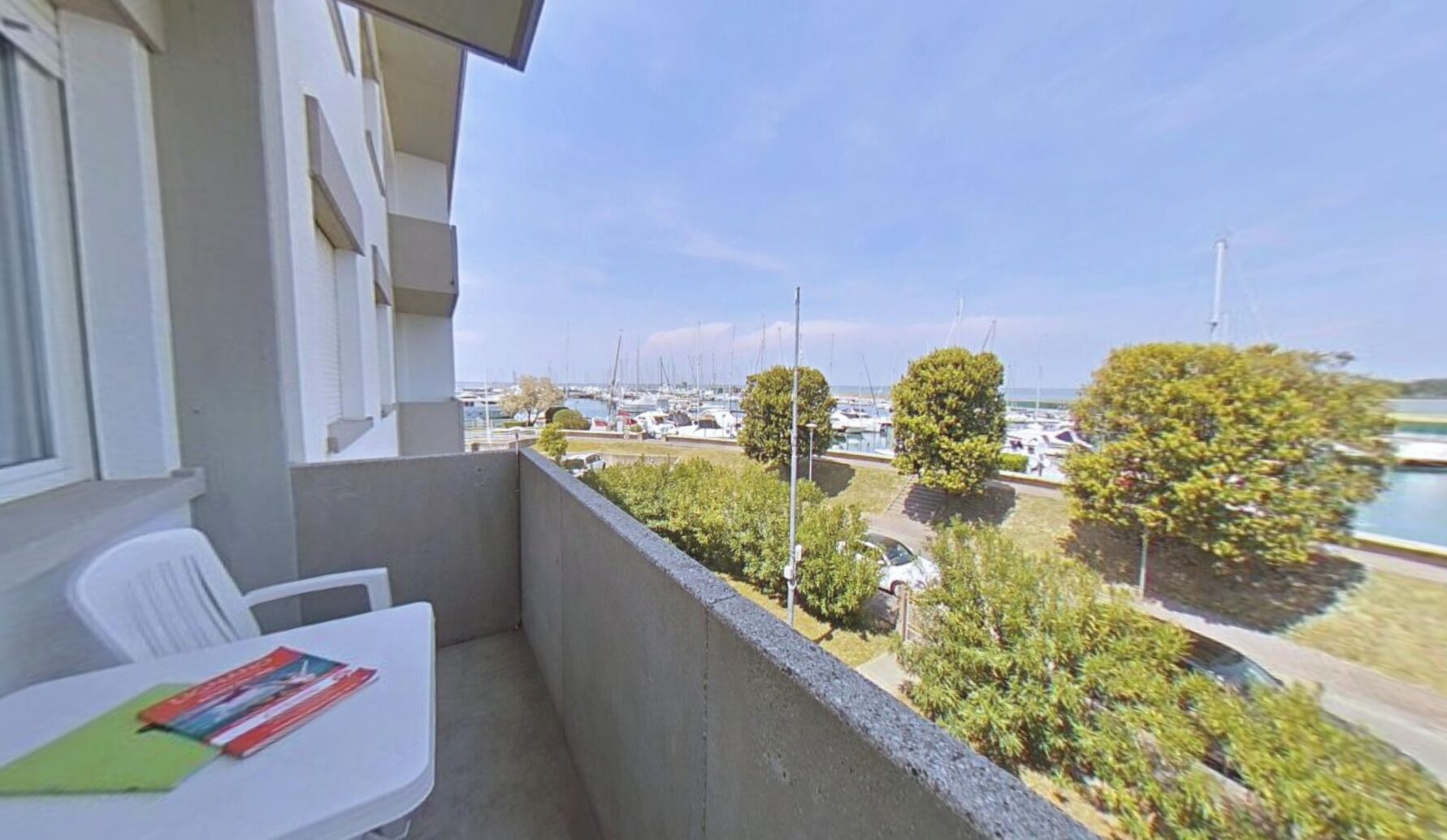 A balcony with a view of a marina, a white table with a book, and a chair.