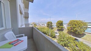 Un balcón con vistas a un puerto deportivo, una mesa blanca con un libro y una silla.
