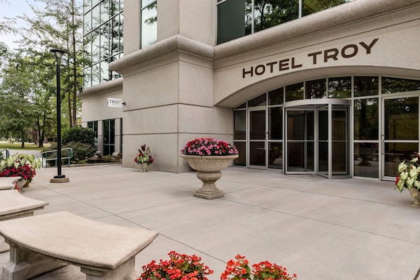 Entrada de un hotel con un letrero que dice 'HOTEL TROY' y una puerta giratoria.