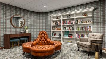 Ein Zimmer mit Ledersessel, Bücherregal, rundem Spiegel und kleinem Schreibtisch.