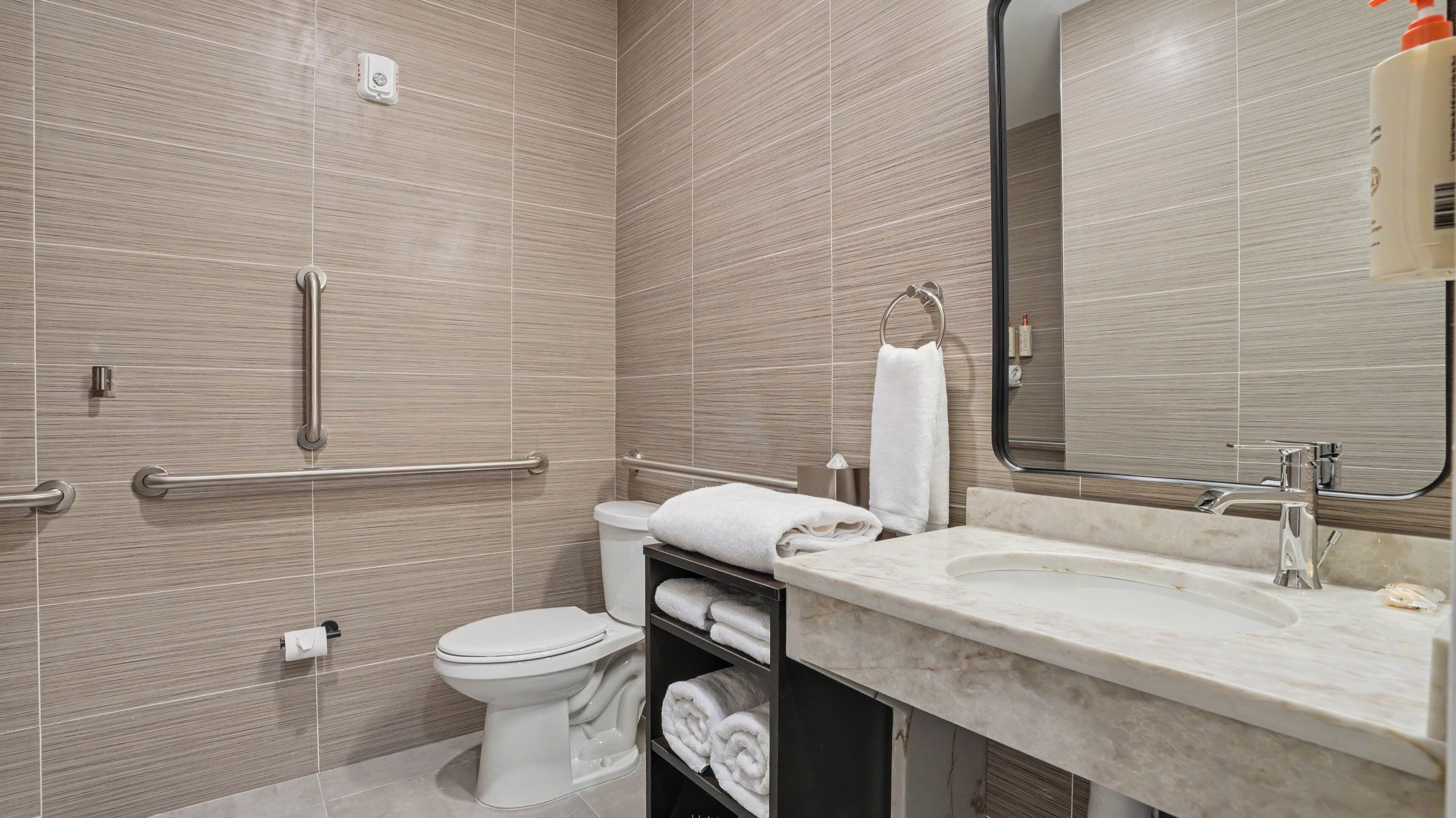 A modern bathroom with a toilet, sink, and handrails.