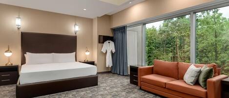 Une chambre d’hôtel avec un grand lit, un canapé, un bureau et une vue sur les arbres par la fenêtre.
