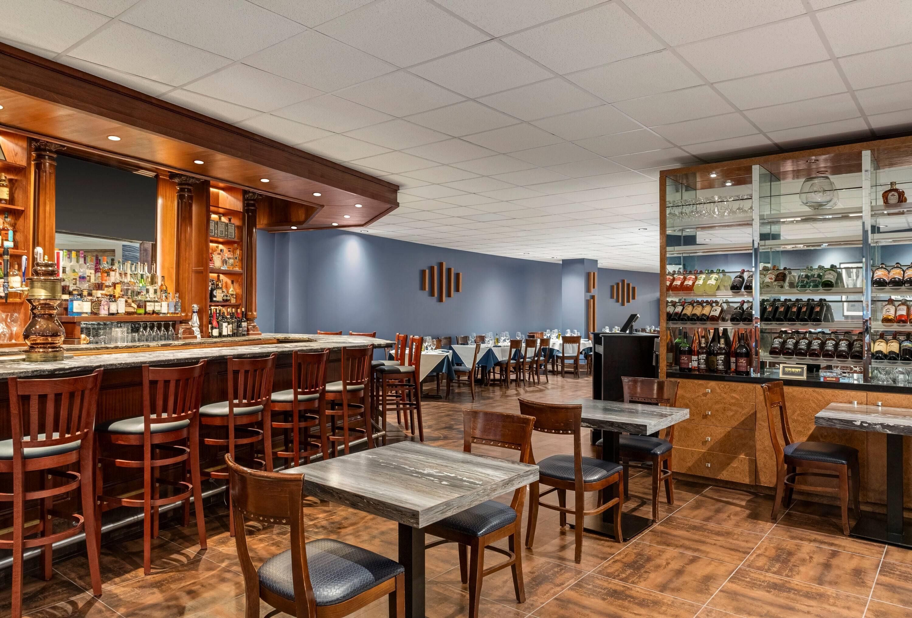 Eine Bar mit Holztischen und -stühlen, einer Theke mit Flaschen und einer Weinauslage.