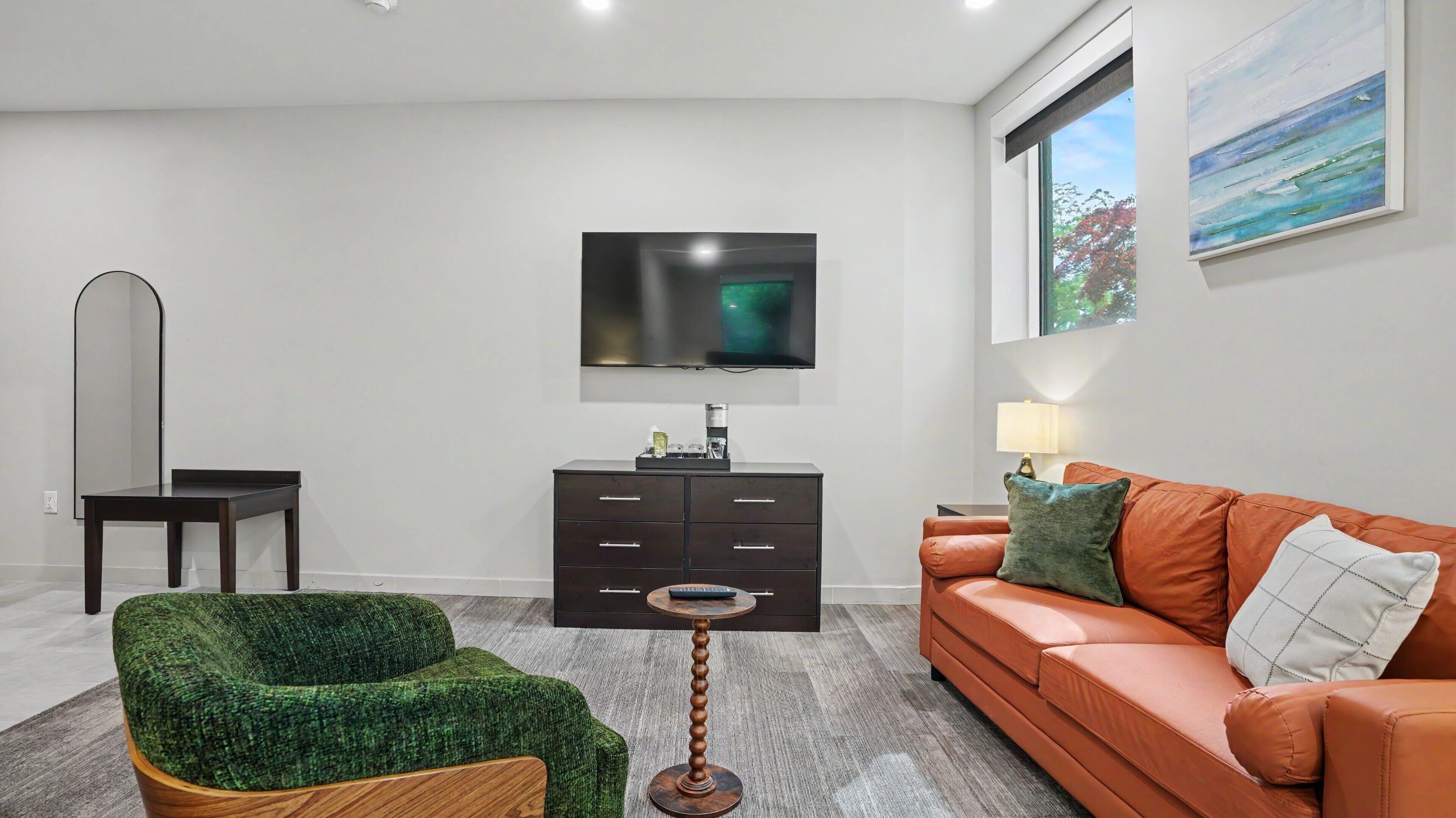 A modern living room with a sofa, a green armchair, a coffee table, a TV, and a painting.