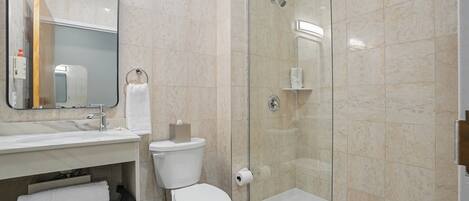 A bathroom with a toilet, sink, mirror, towel rack, and a glass-enclosed shower area.