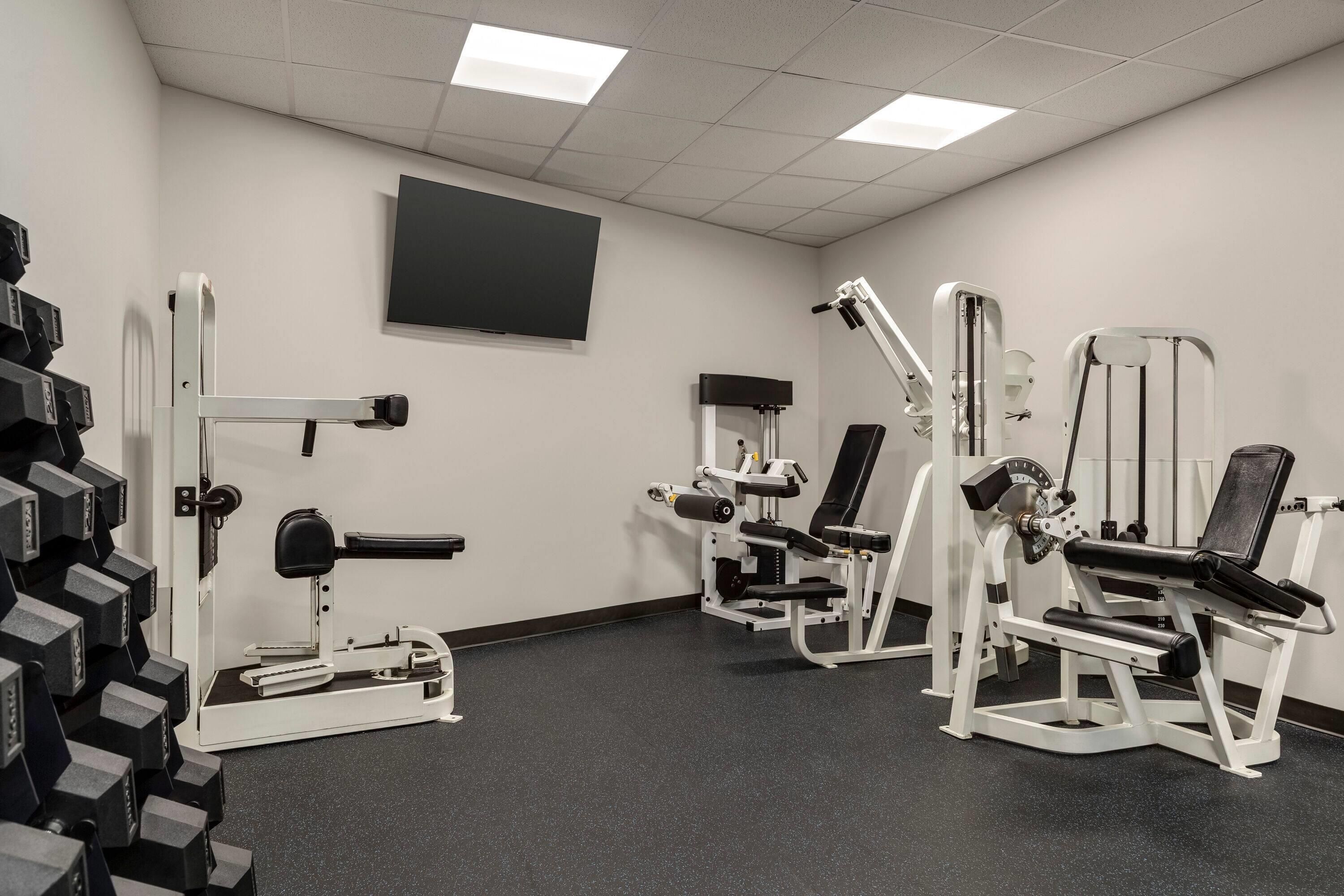 Un gimnasio con diversas máquinas de ejercicio, un televisor de pantalla plana en la pared y suelo de goma negra.