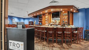 Un espace bar comprenant un comptoir, des tabourets de bar et des étagères remplies de bouteilles.