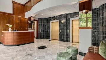 Een hotel lobby met een receptiebalie, liften, marmeren vloeren en een groot raam.