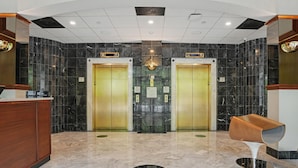 Un hall d’entrée avec un sol en marbre, deux ascenseurs, un comptoir de réception et un fauteuil moderne.