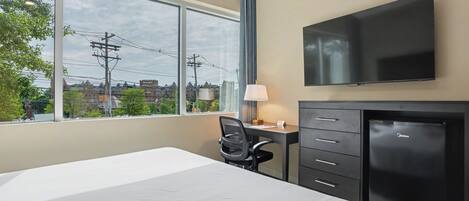 Une chambre d’hôtel équipée d’un lit, d’un bureau, d’une chaise, d’une télévision et offrant une vue sur les bâtiments et les lignes électriques.