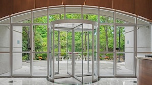 Une porte tournante à panneaux de verre, donnant sur un espace extérieur agrémenté d’arbres et d’un chemin pavé.