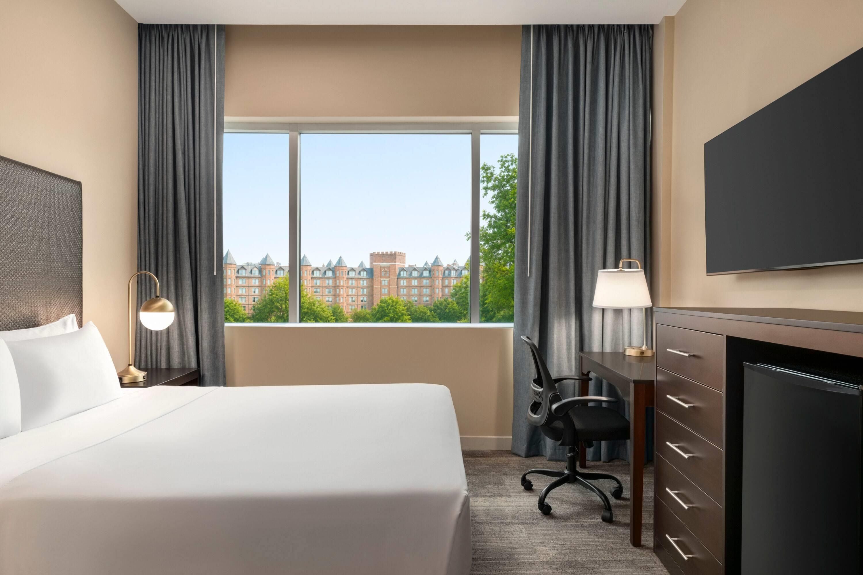 Une chambre d’hôtel avec un grand lit, un bureau, une chaise, une télévision et une fenêtre donnant sur la ville.