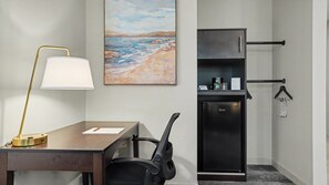 A hotel room with a desk, chair, lamp, refrigerator, and artwork on the wall. - Hotel Troy, Trademark Collection by Wyndham (Parsippany)
