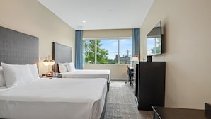Une chambre d’hôtel avec deux lits, un bureau, une chaise, une télévision et une grande fenêtre donnant sur la ville.