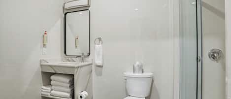 Un baño con inodoro, lavamanos con espejo, cabina de ducha de cristal y un perchero para toallas.