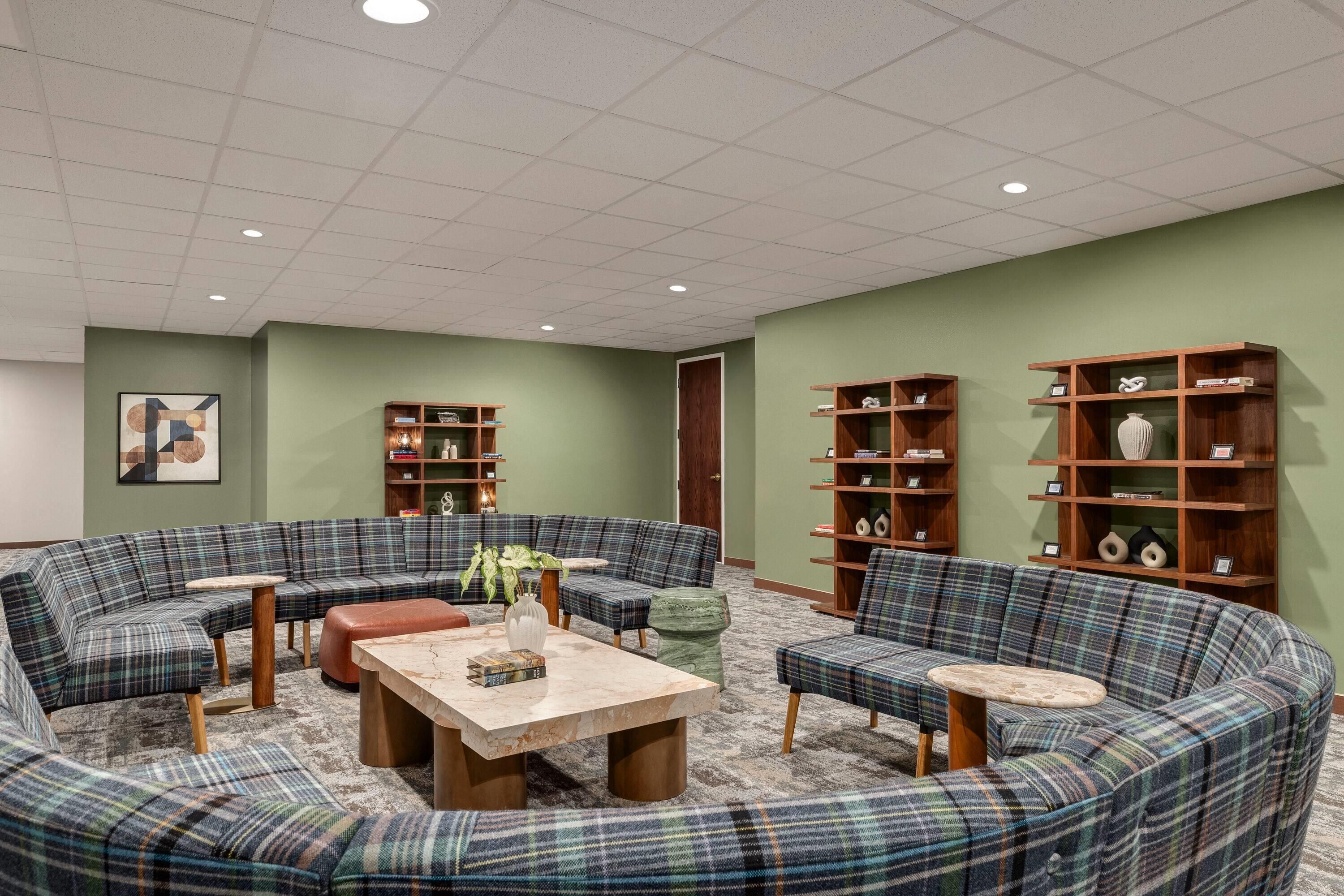 A cozy lounge area with a large, curved sofa set, a coffee table, and two side tables. There are two wooden bookshelves filled with books and decorative items.