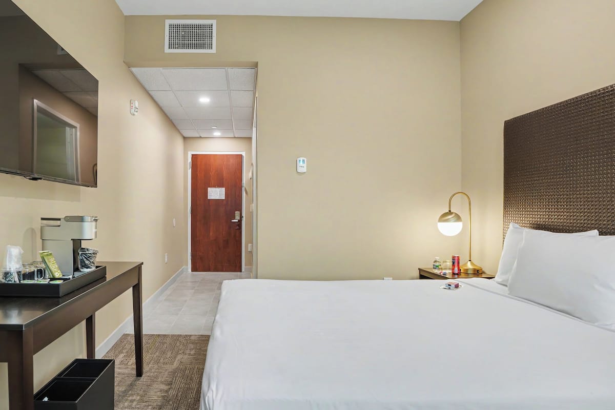Una camera d'albergo con un letto, un comodino, una lampada, una TV e una porta che dà su un'altra stanza.