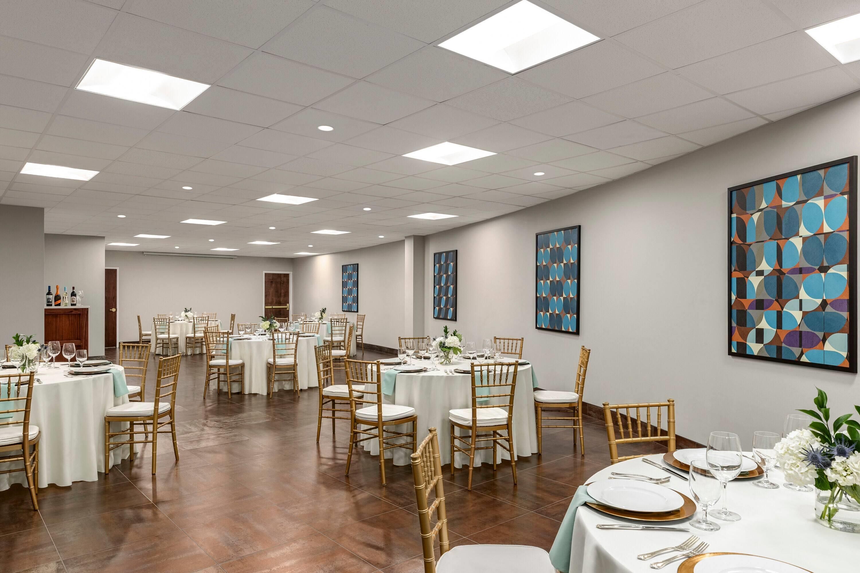 A banquet hall with round tables, chairs, and artwork on the walls.
