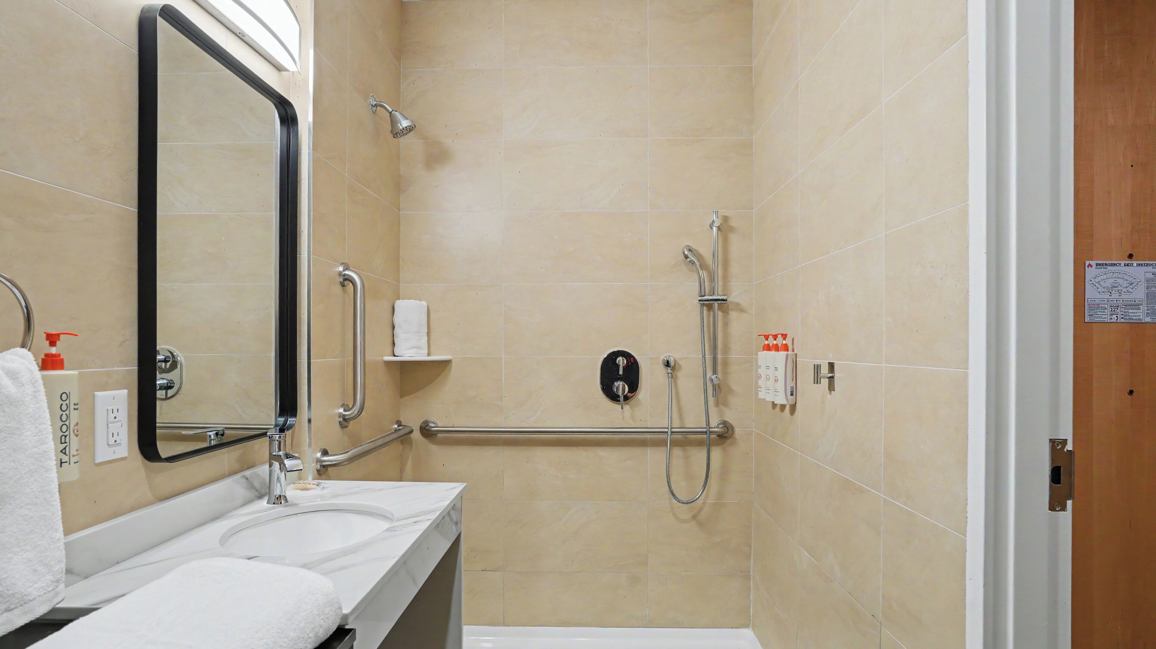 A bathroom with a sink, mirror, towel rack, and a shower with grab bars.