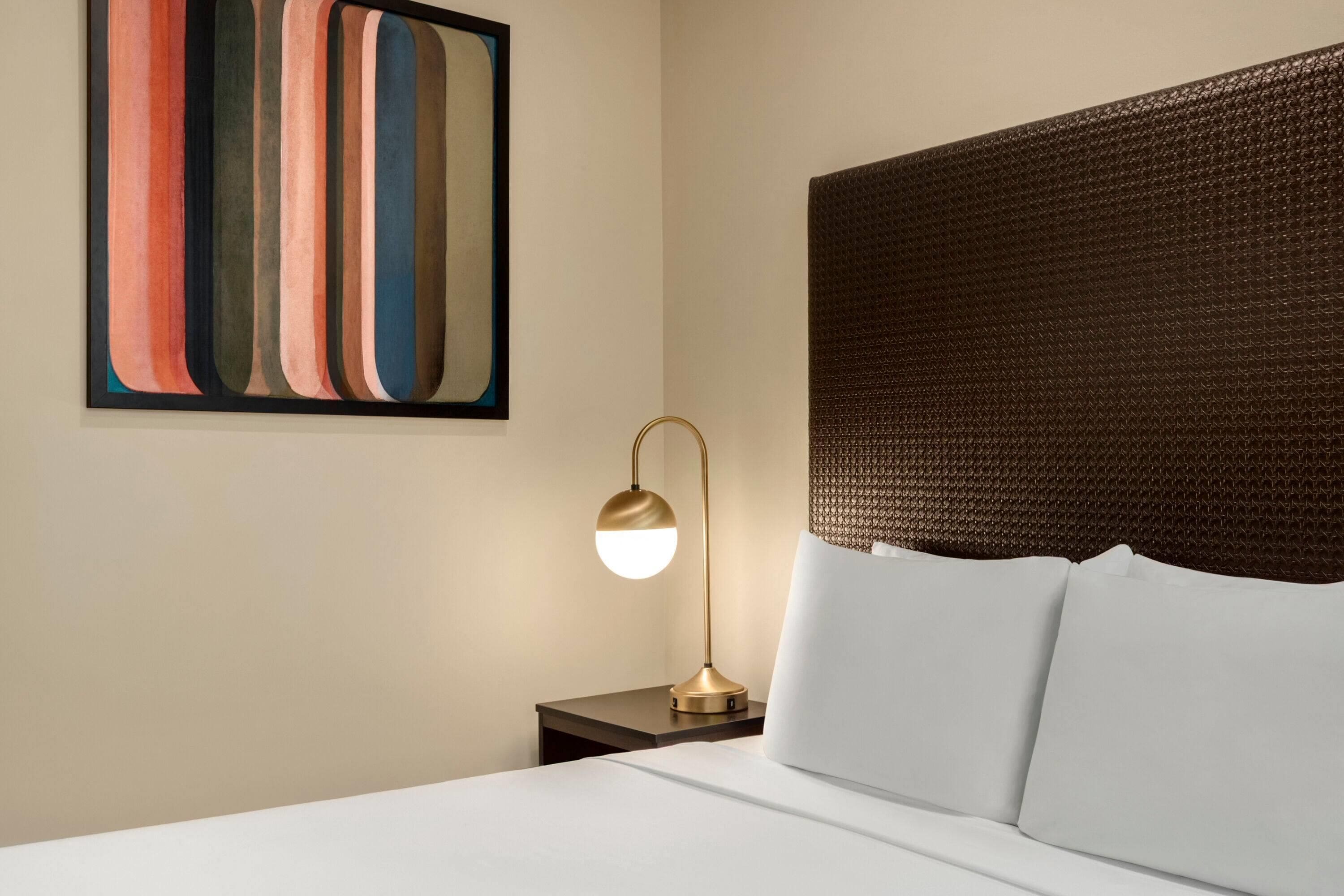 Une chambre d’hôtel avec un lit, une table de chevet, une lampe et une œuvre d’art murale.