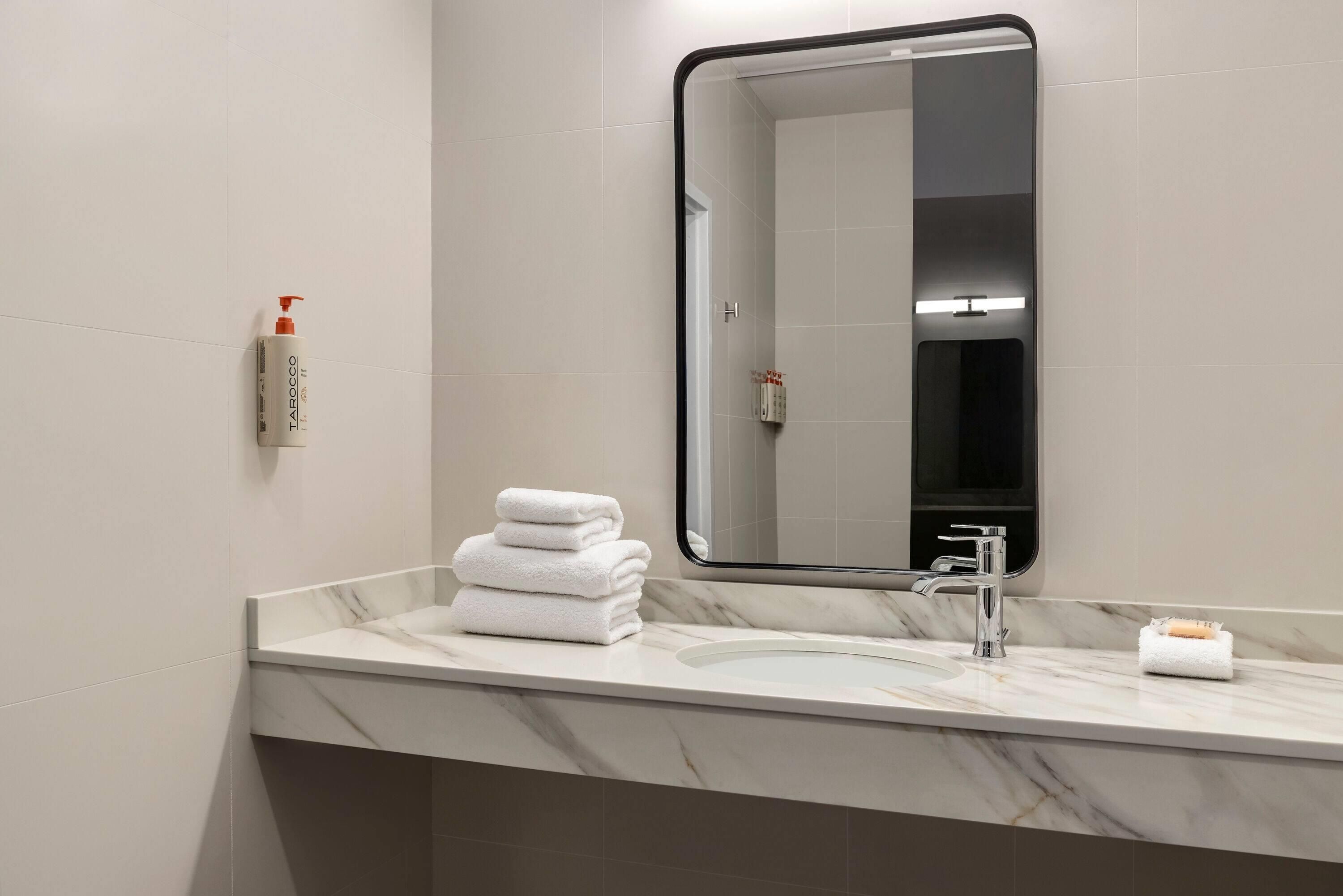 Une salle de bain avec un comptoir en marbre, un lavabo, un miroir et une pile de serviettes blanches.