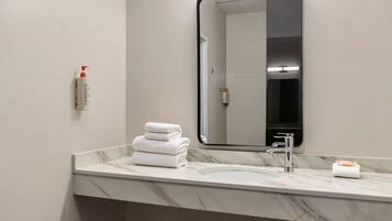 Une salle de bain avec un comptoir en marbre, un lavabo, un miroir et une pile de serviettes blanches.