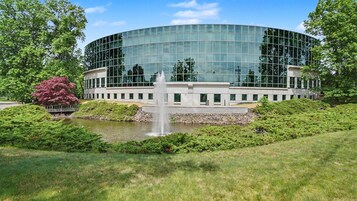 Un edificio moderno con fachada de vidrio circular, una fuente central y vegetación circundante.