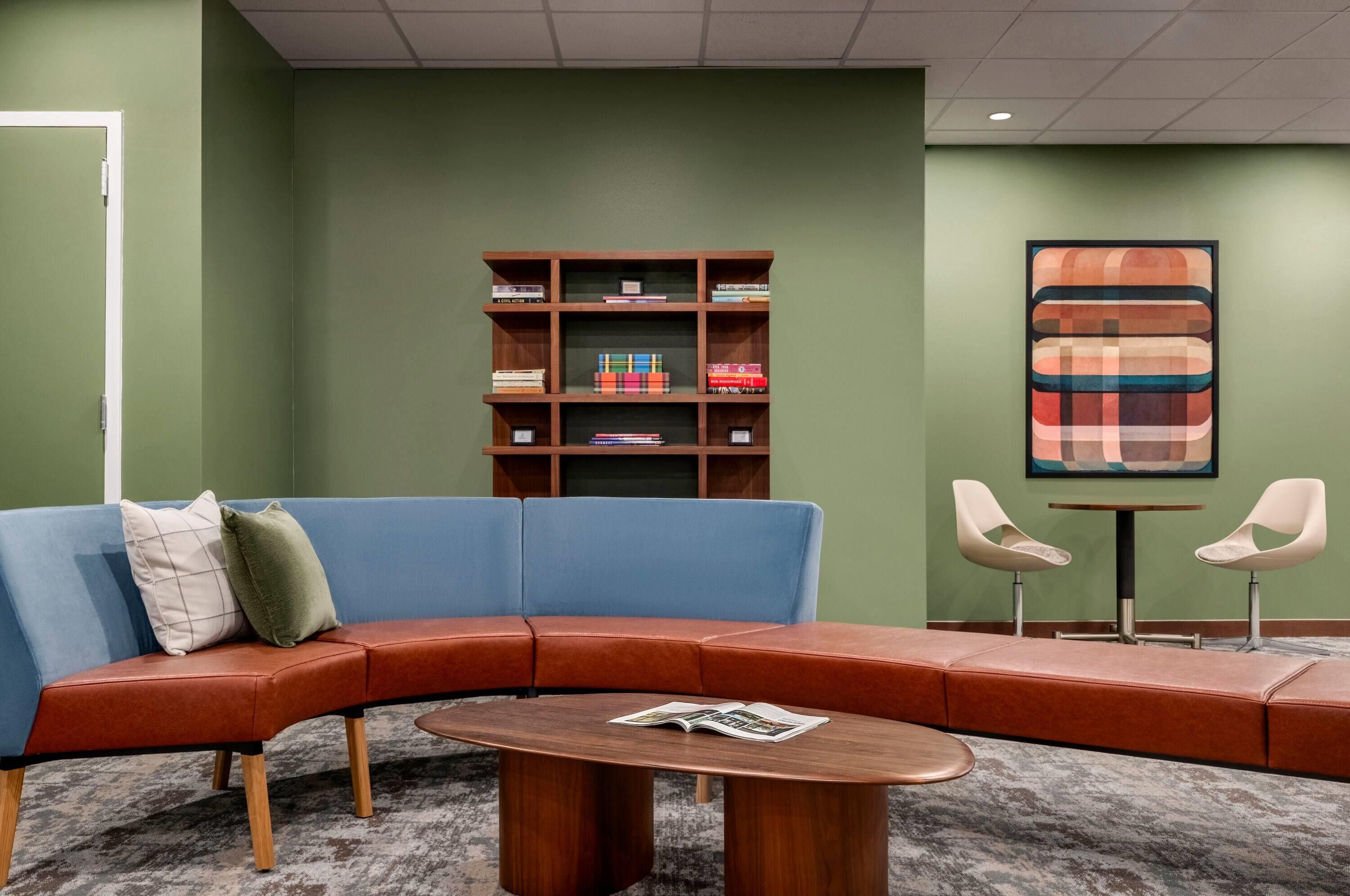 A modern lounge area with a curved sofa, a coffee table, and a bookshelf against a green wall.