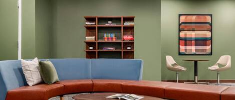A modern lounge area with a curved sofa, a coffee table, and a bookshelf against a green wall.
