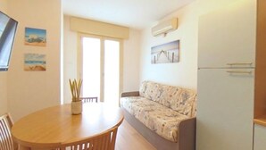 A compact living space with a sofa, a dining table, and a refrigerator. - Cozy central flat 150mt from the beach (Lignano Sabbiadoro)