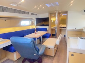 A compact interior with a dining area, a seating bench, a small table, and a kitchenette. - Caribbean Dream: Sun-soaked Sailing Adventure from Tortola, Islas Vírgenes Británicas (Road Town)