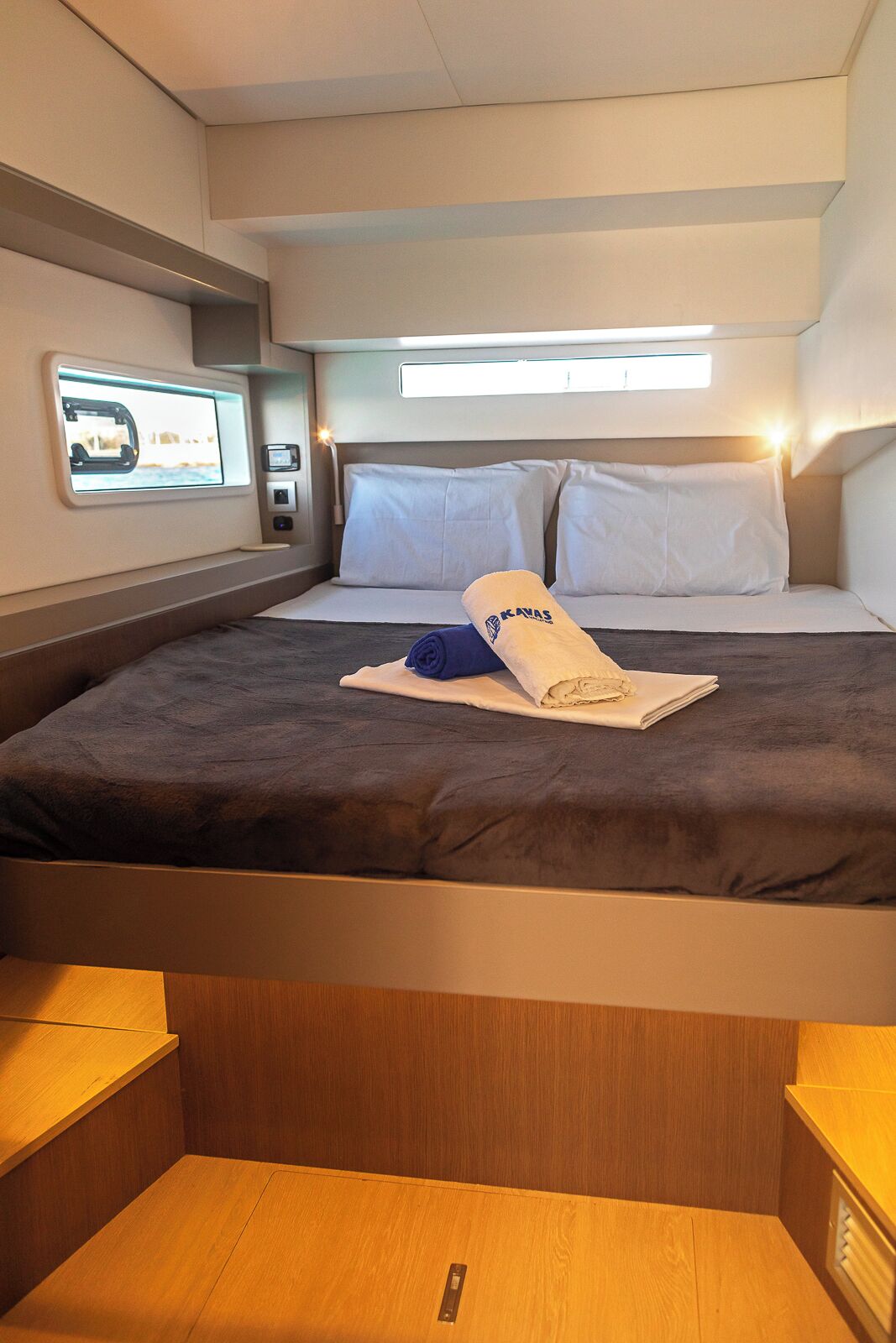 Une cabine compacte et bien éclairée, équipée d’un lit, d’oreillers, d’une petite table et d’un panneau de commande.